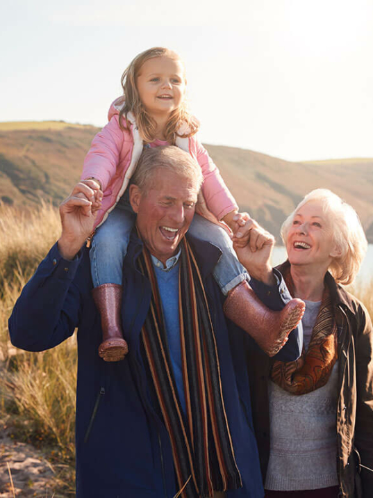 Grandparents walking beside a lake with their grand-daughter on Grandpa's shoulders