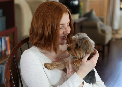 Hannah, a college student, smiling and holding her small dog in her arms