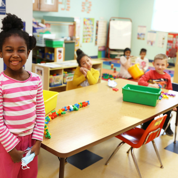 A happy, proud little girl standing in front of her classmates playing behind her